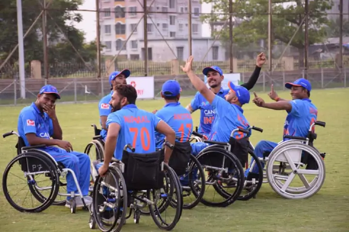 Para-athletes in blue jerseys and wheelchairs celebrating together on a sports field